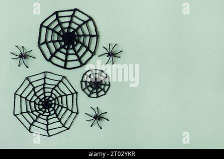Happy Halloween holiday concept. Knitted black spider web and small spiders on a green background. Halloween greeting card mockup with copy space. Fla Stock Photo