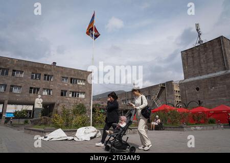 A family walks past the flag of the Republic of Nagorno-Karabakh in the main square of Goris. Armenia reported on the 3rd October that around 100,625 refugees have arrived from Nagorno-Karabakh while 91,924 of them have been already registered by Armenian officials after Azerbaijan took control of the southern mountainous region. Stock Photo