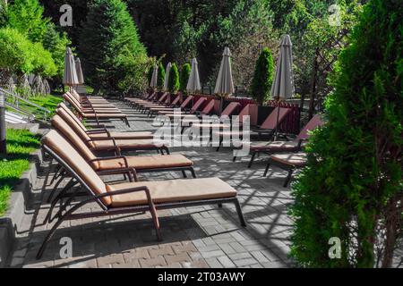 Empty sun loungers stand in recreation area for tourists and vacationers. Empty sun loungers are located in pool area. End of tourist season. Pandemic and isolation. Lack of tourists. Stock Photo