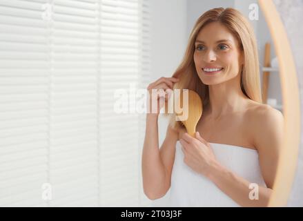 Beautiful woman brushing her hair near mirror in bathroom, space for text Stock Photo