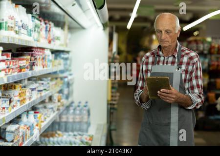 Senior male supermarket owner using a digital tablet while standing in his grocery store. Old successful entrepreneur running small business using Stock Photo