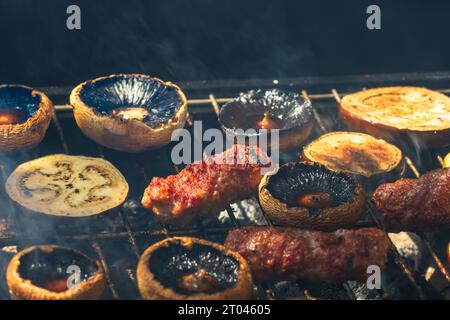 Grilling meat rolls called mici or mititei with vegetables on char barbecue. Charcoal grill with burning fire Stock Photo