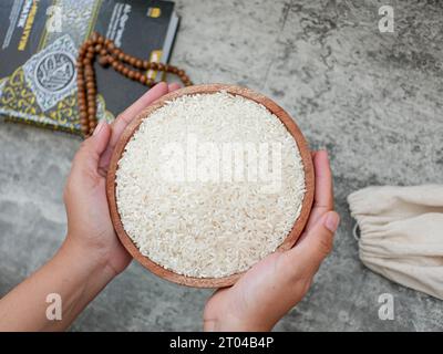Hand holding wooden bowl filled with rice grains for zakat, concept of zakat in Islamic religion. Muslims help the poor and the needy. Stock Photo