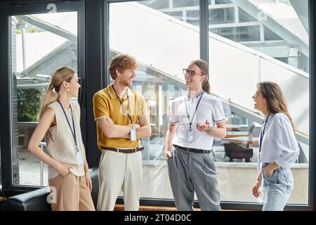 four young employees in smart casual outfits smiling sincerely discussing work, coworking concept Stock Photo
