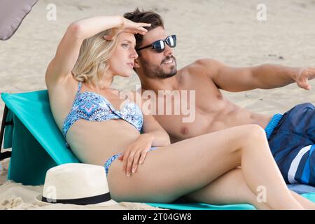 couple sunbathing on beach pointing towards the sea Stock Photo