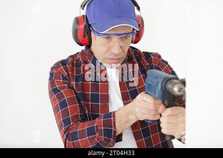 mature man wearing protective equipment using cordless screwdriver Stock Photo