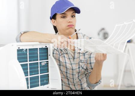 tired female repairwoman repairing ceiling air conditioning unit Stock Photo