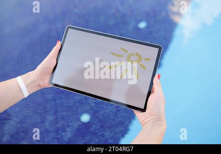 Female hands hold tablet with drawn sun and white screen above pool Stock Photo