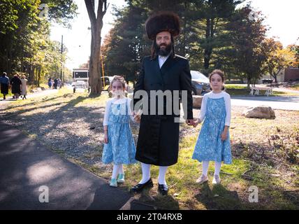 Portrait of a Hasidic Jewish man in a shtreimel fur hat holding hands with his 2 similarly dressed daughters, Entering Manny Weldler Park in Monsey NY. Stock Photo