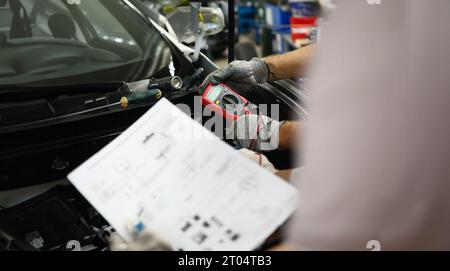 Mechanical service using multimeter to check voltage level in car battery and auto documentation diagram Stock Photo