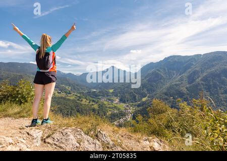 Cheerful girl hiker celebrating her success with raised outstretched arms, enjoying mountain scenery in the summer season. Challenge, goal, and Stock Photo