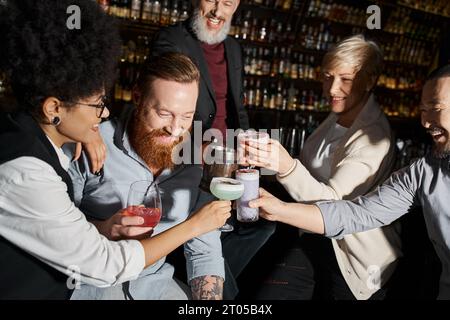 diverse team of cheerful multicultural friends clinking glasses while having fun in cocktail bar Stock Photo