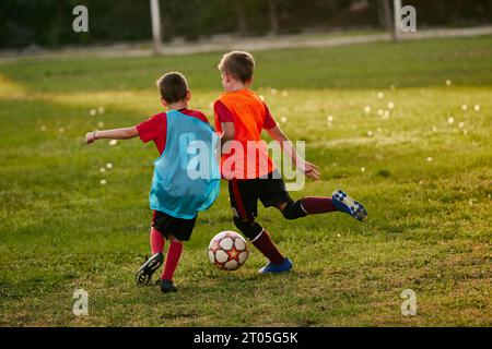 Back view competitive boys, player running wearing sport uniform in jersey and cleats. Kids play football on soccer field. Children's school team. Stock Photo