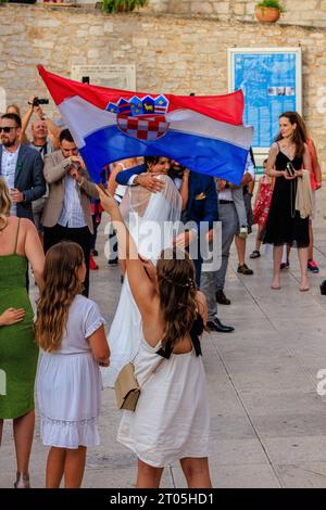 a young girl waves the croatian flag as a bride in white wedding dress hugs and celebrates in the cathedral square in sibenik croatia Stock Photo