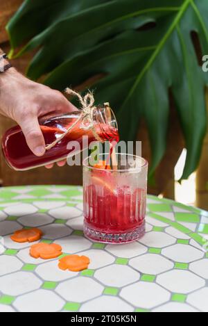 Hand pouring healthy mixed juice made of carrot, orange fruit, pink dragon fruit, apple with glass with ice Stock Photo