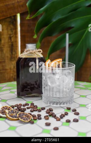 Cold brew coffee in a bottle with transparent glass full of ice on green leaves background Stock Photo