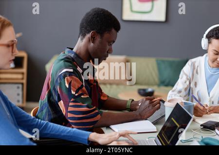 Side view portrait of young Black man using digital tablet while working with team at table, copy space Stock Photo