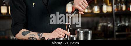 cropped view of bartender pouring alcohol drink into jigger near cocktail shakers in bar, banner Stock Photo