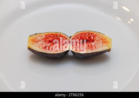 Two halves of a ripe sliced fig on a white plate photographed in studio Stock Photo