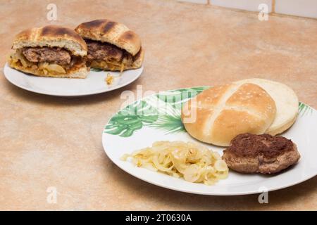 A mouthwatering toasted hamburger patty, bread, and golden onions in the foreground on a plate. In the background, a split hamburger reveals its juicy Stock Photo