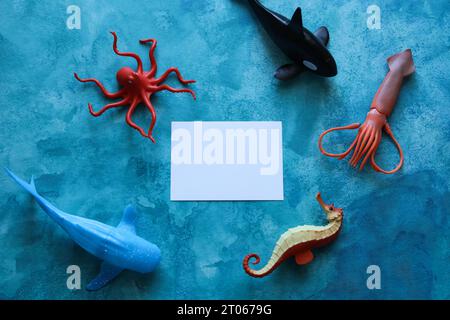 a close up of a blank note card with sea life animal toys on a blue watercolor background Stock Photo