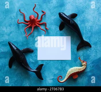 a close up of a blank note card with sea life animal toys on a blue watercolor background Stock Photo