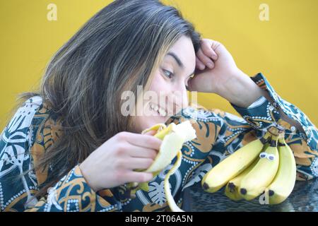 laughing woman eating banana, yellow background Stock Photo