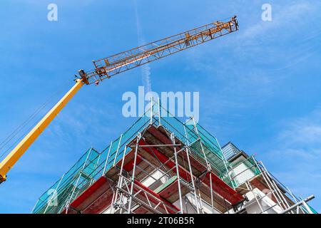 Part of a building surrounded by scaffolding and the boom of a construction crane against the blue sky. Stock Photo