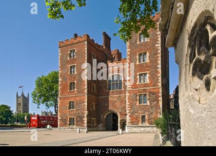 Lambeth Palace London. Morton's Tower red brick Tudor gatehouse forming the Tudor historic entrance to Lambeth Palace, with Houses of Parliament and open tour bus behind. London UK Stock Photo