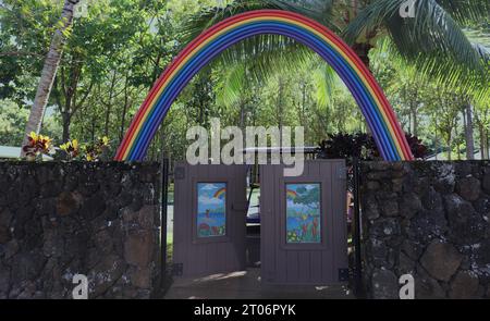 The entrance to the Children's Play Area at Na Aina Kai Botanical Gardens with a rainbow over two wood doors with mosaics attached to walls made from Stock Photo