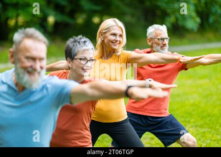 Group of senior people practicing yoga outdoors, standing in Warrior two pose Stock Photo