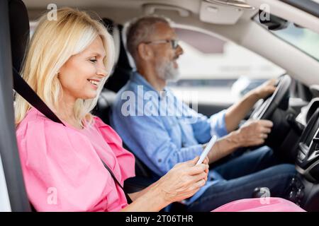Happy elderly woman using smartphone while riding car with husband Stock Photo