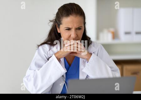 Serious concentrated mature woman doctor looking at laptop screen Stock Photo