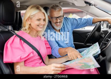 Retired man and woman travelers sitting inside auto, reading map Stock Photo
