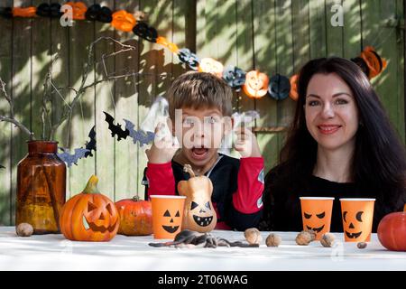 Portrait mother and son on sunny autumn day against background of old wooden wall. Family mother and son are preparing for Halloween, decorating yard Stock Photo
