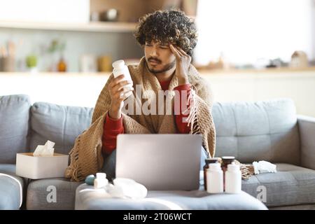 Sick Indian Man Holding Bottle With Pills While Sitting At Home Stock Photo
