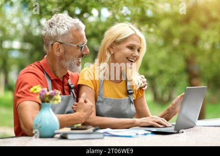 Happy Mature Spouses Shopping Online On Laptop While Sitting In Their Garden Stock Photo