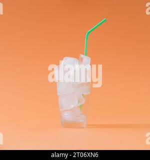 Creative composition made of empty glass full of ice cubes with green drinking straw on pastel orange background. Minimal diet no calories concept. Stock Photo