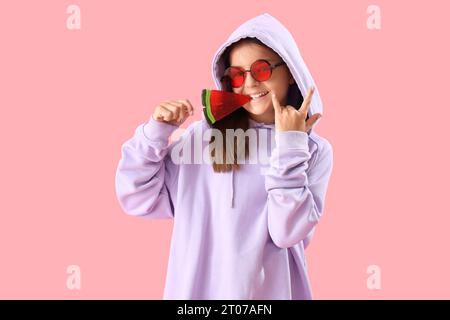 Happy little girl with lollipop in shape of watermelon slice showing 'devil horns' on pink background Stock Photo