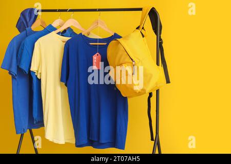 Rack with t-shirts, cap and backpack on yellow background. Black Friday sale Stock Photo