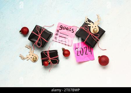 Sticky notes with different goals for 2024, gift boxes and Christmas decorations on gradient background Stock Photo