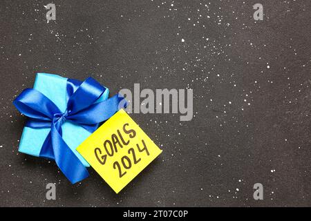 Sticky note with goals for 2024 and gift box on grunge black background Stock Photo