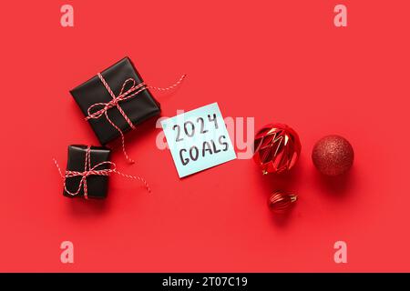 Sticky note with goals for 2024, gift boxes and Christmas balls on red background Stock Photo
