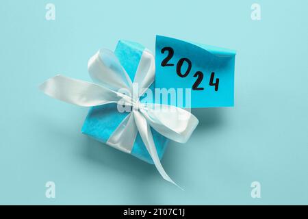 Sticky note with year 2024 and gift box on blue background Stock Photo