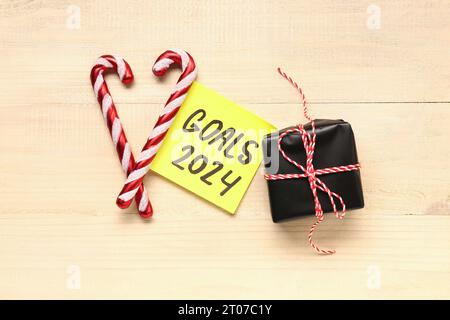 Sticky note with goals for 2024, gift box and candy canes on beige wooden background Stock Photo