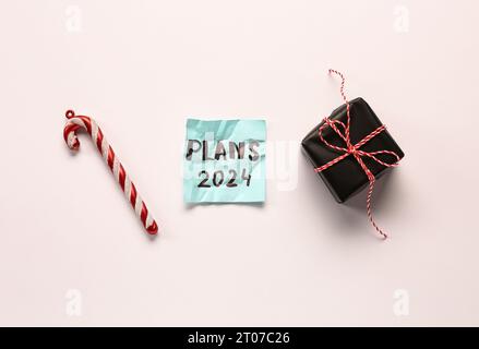 Sticky note with goals for 2024, gift box and candy cane on white background Stock Photo
