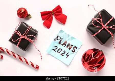 Sticky note with goals for 2024, gift boxes and Christmas decorations on white background Stock Photo