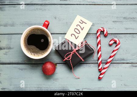 Sticky note with year 2024, gift box, cup of coffee and Christmas decorations on grey wooden background Stock Photo