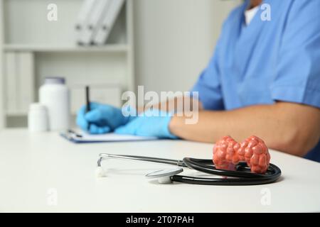 Endocrinologist working in hospital, focus on thyroid gland model and stethoscope on white table Stock Photo
