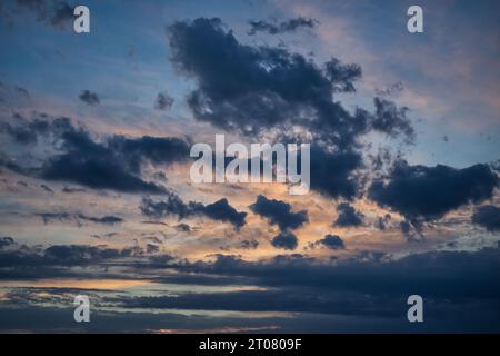 Orange and pink sky with a setting sun behind a layer of fluffy white clouds. The sun casts warm rays tinged with colors of the evening sky onto the h Stock Photo